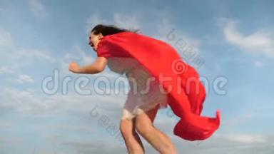 开朗的年轻女子扮演超级<strong>英雄</strong>。 快乐的超级<strong>英雄</strong>女孩穿着红色斗篷跑着笑着，斗篷在风中飘扬
